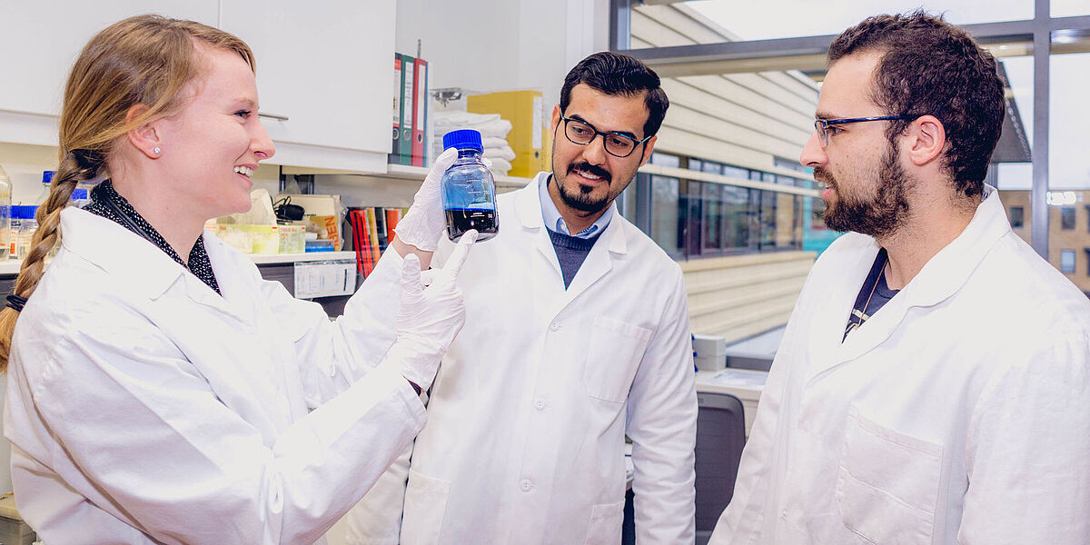 Three doctoral students stand in a lab and talk to each other