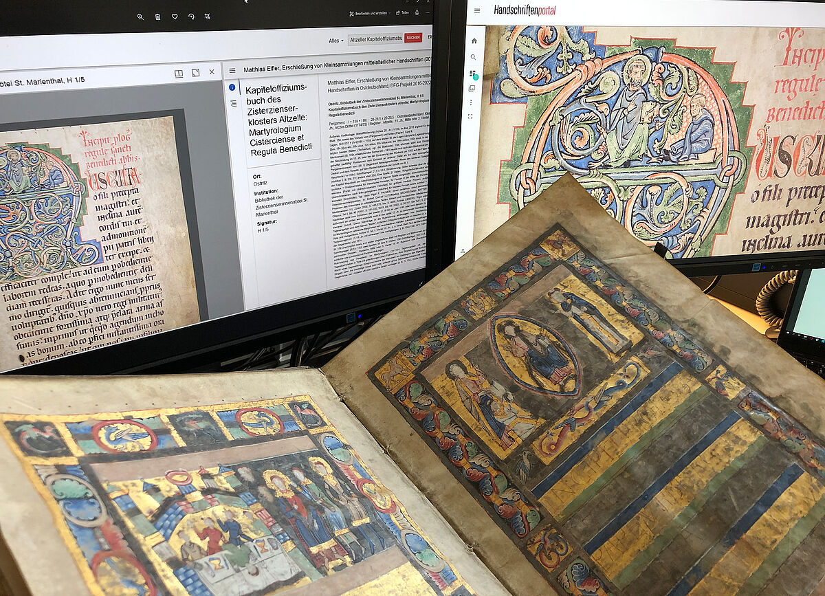 Auf dem Bild sind mittelalterliche Handschriften vor einem Computer zu sehen. Auf dem Monitor ist die gescannte Seite mit Metadten zu sehen.
