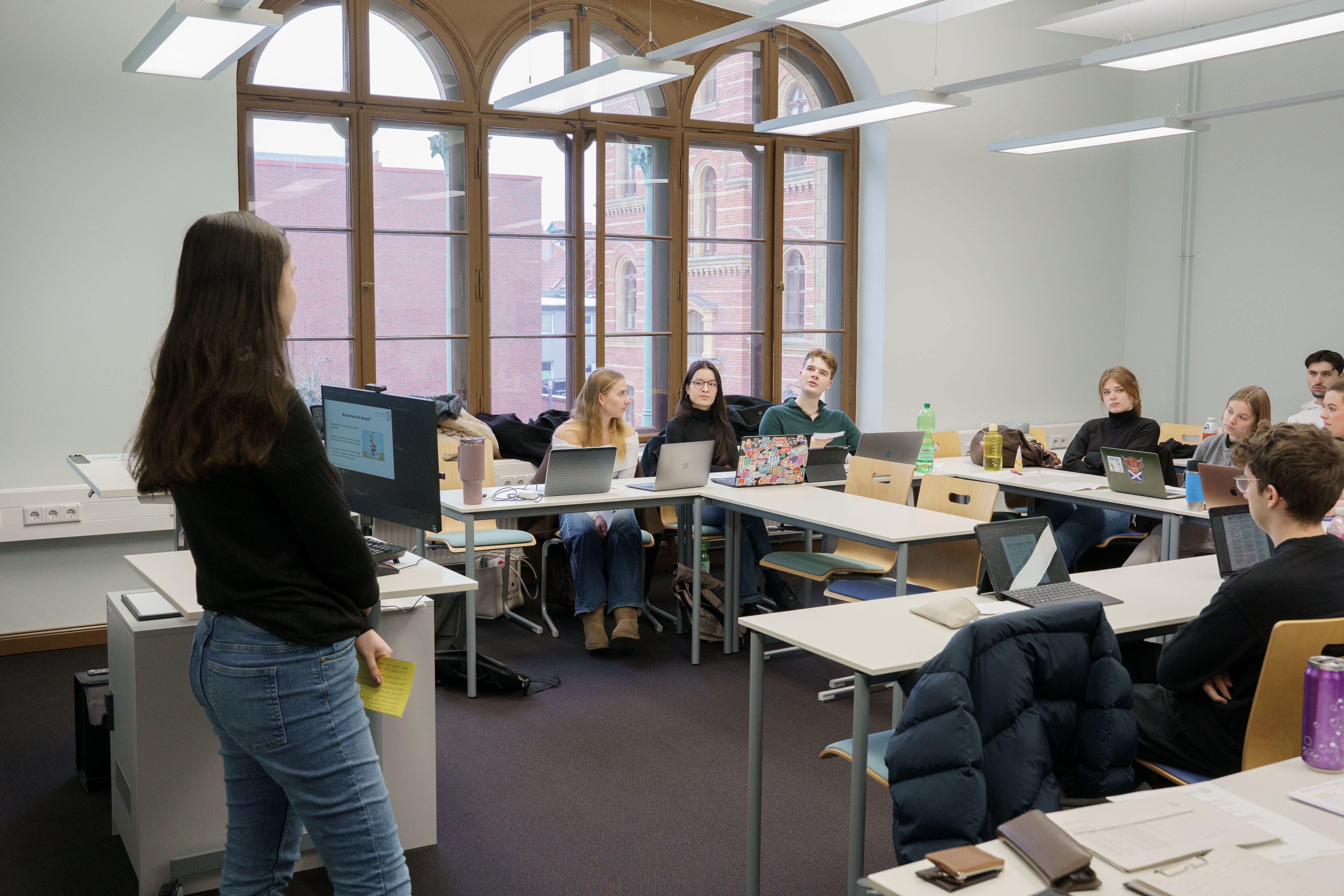 Mehrere Personen hören in einem Seminarraum einer jungen Frau am Pult zu.