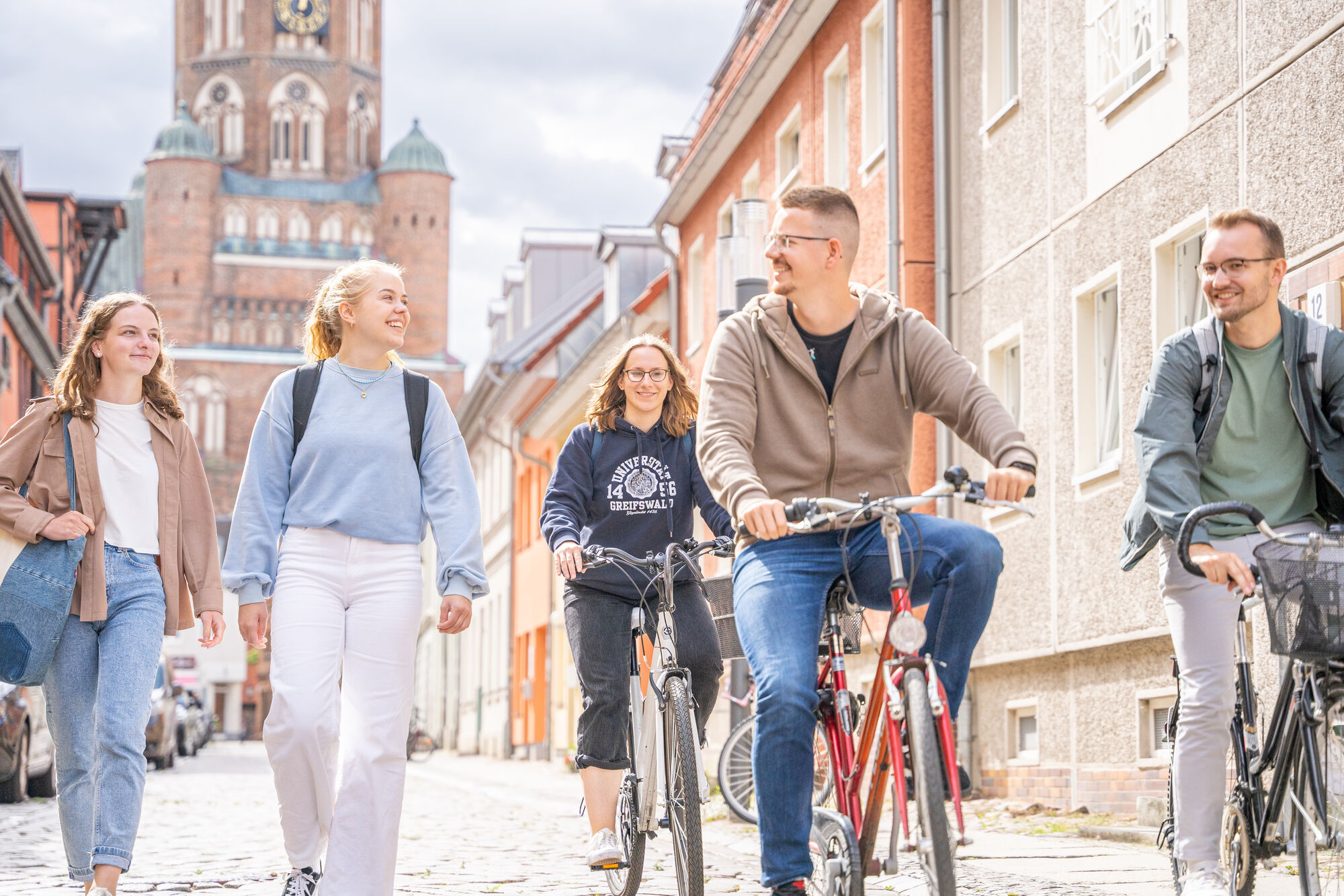 Studierende gehen zu Fuß durch die Hunnenstraße Richtung Campus Loefflerstraße. Im Hintergrund ist der Dom zu sehen.