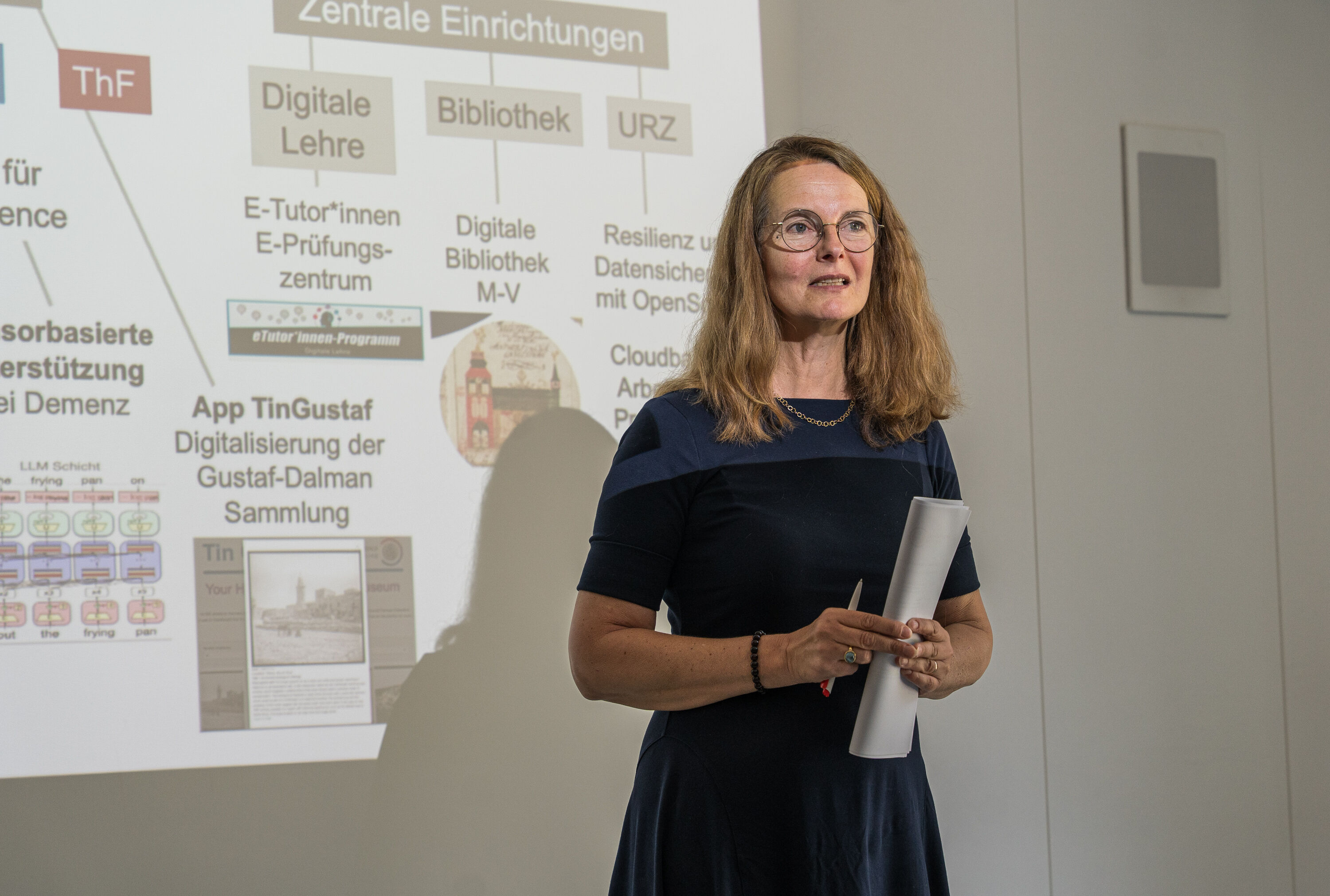 Bettina Martin (Wissenschaftsministerin MV) hält ein Grußwort bei der Eröffnung von CEDAR Eine Frau steht vor einer Präsentation und hält eine Ansprache