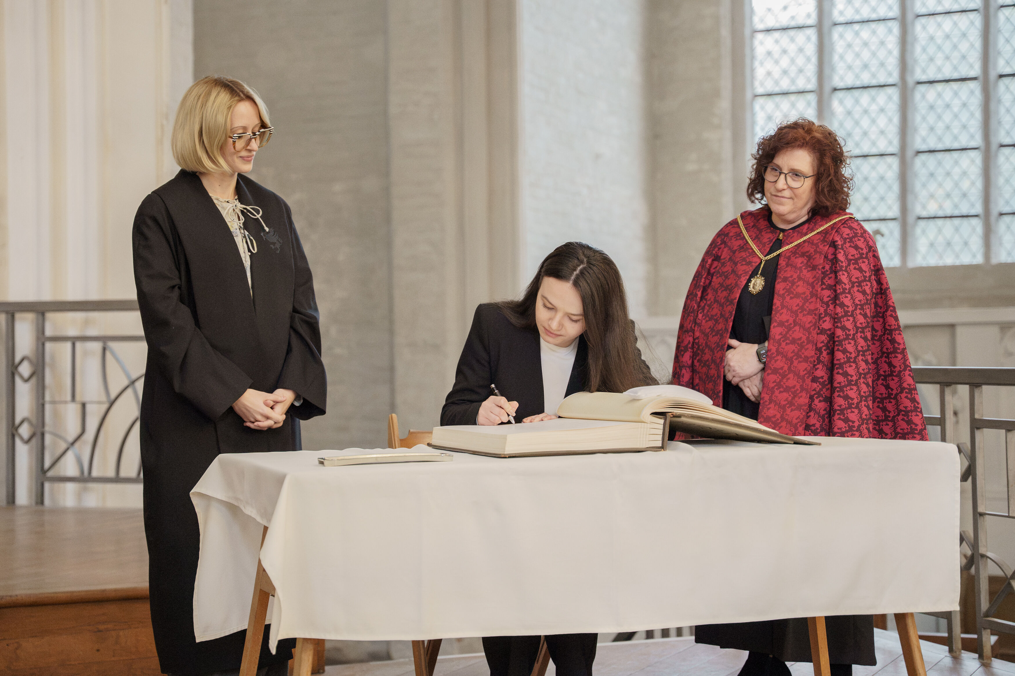 Einschreibung in das Ehrenbuch der Universität Eine junge Frau schreibt sich in ein alten großes Buch in einer alten Kirche ein.
