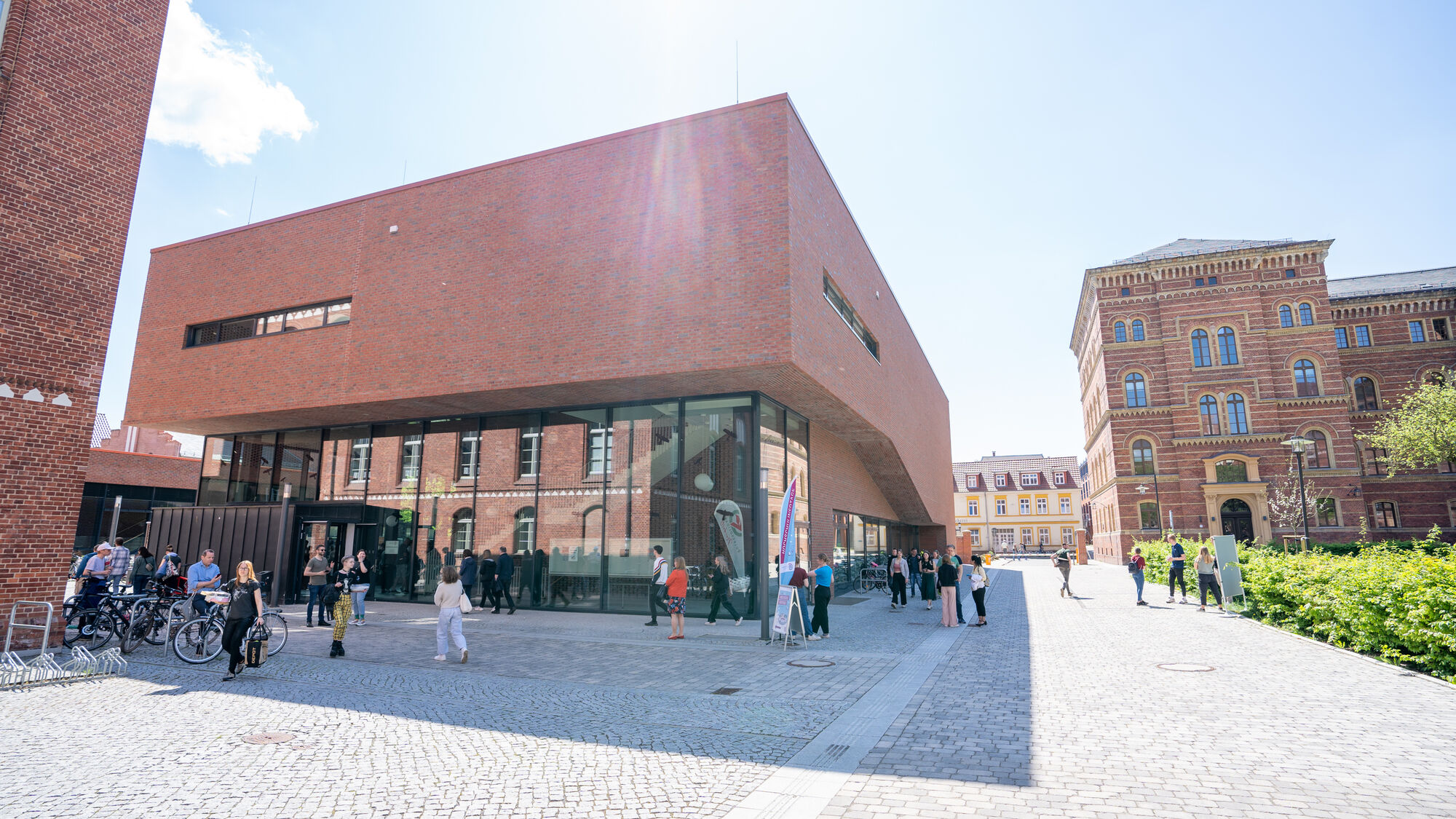 Neues Audimax Campus Loefflerstraße Viele Personen laufen um das Neue Audimax auf dem Campus Loefflerstraße. Zu sehen ist ebenfalls das neue Jura-Gebäude.