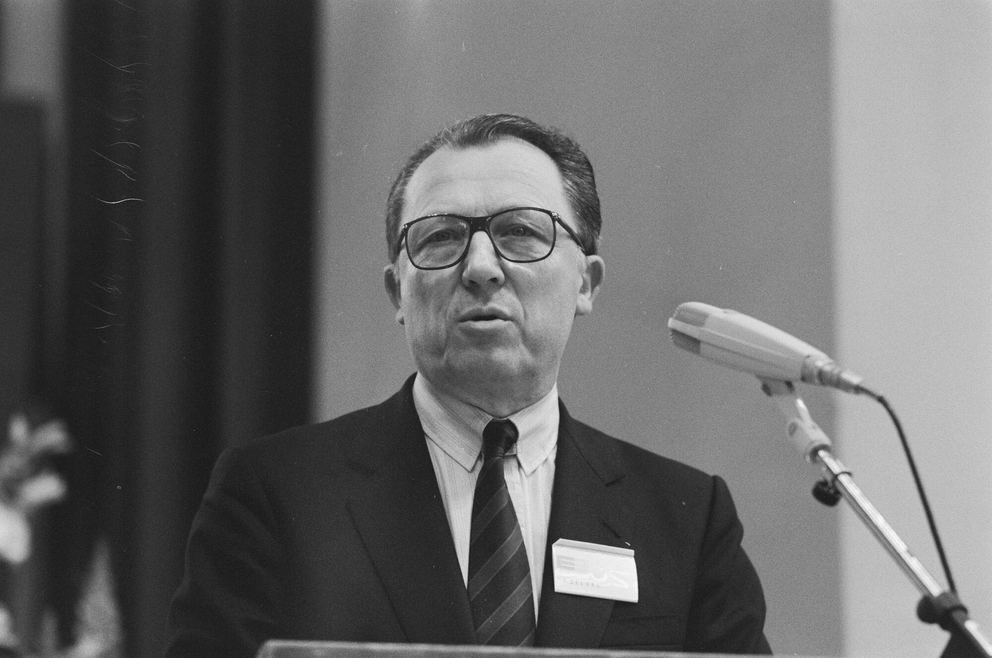 The black and white photo is a portrait of Jacques Delors during a speech. The photo is from 1988 Wikimedia CC0