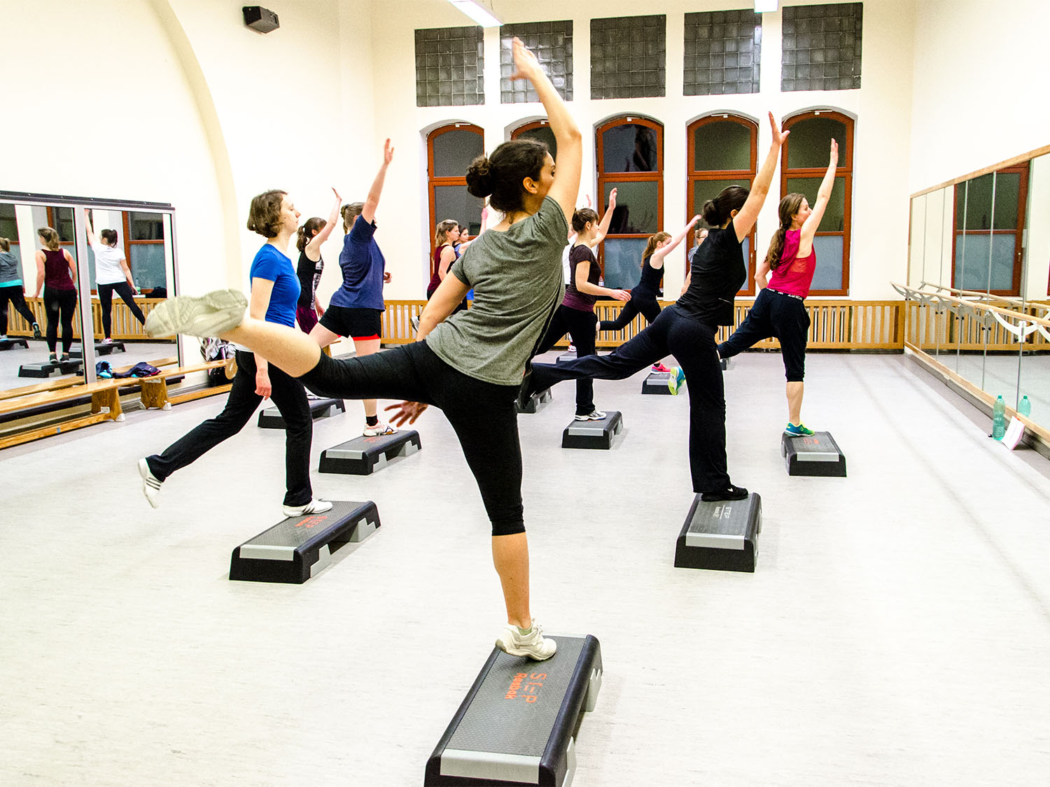 Symbolbild Universitätssport Mehrere Personen bei der Step Aerobic in einer Turnhalle.