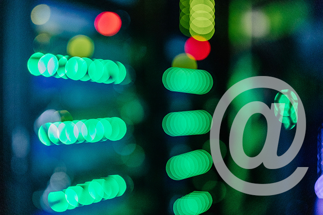 Es leuchten verschwommen bunt blinkende Lichter im Serverraum des Rechenzentrums. Zusätzlich ist ein @ Zeichen aufgedruckt.