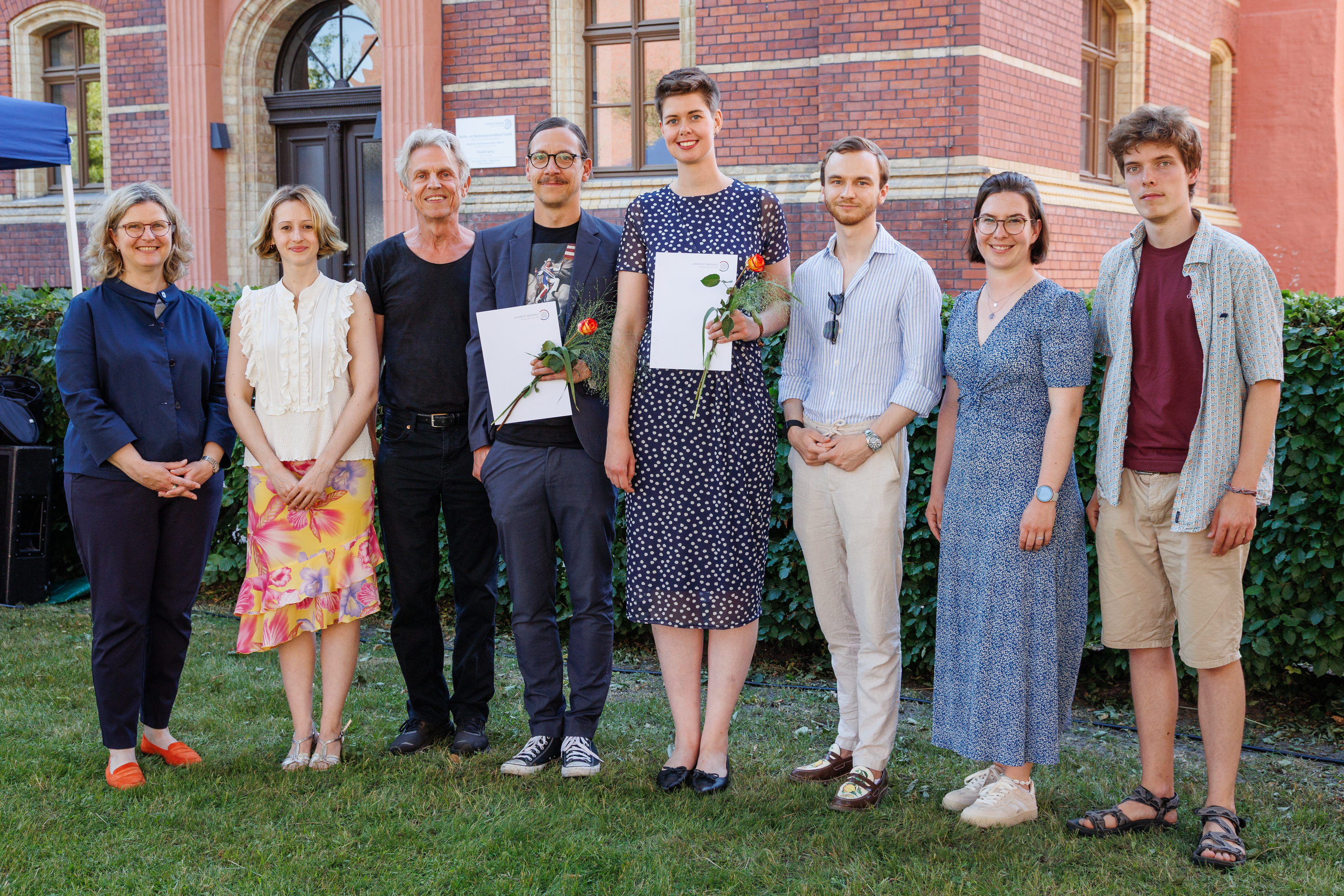 From left to right: Anette Sosna, Patrizia Grenz, Jens Rasmussen, Tobias Gnüchtel, Klara Greffin, and the students who presented the awards at the ceremony during the Dies academicus Several people posing for a group photo on grass with buildings behind them