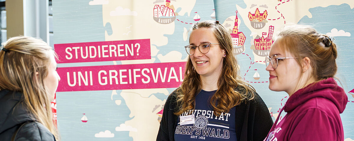 Eine interessierte Personen lässt sich an einem Stand während der Hochschulinformationstage von zwei Studentinnen beraten. 