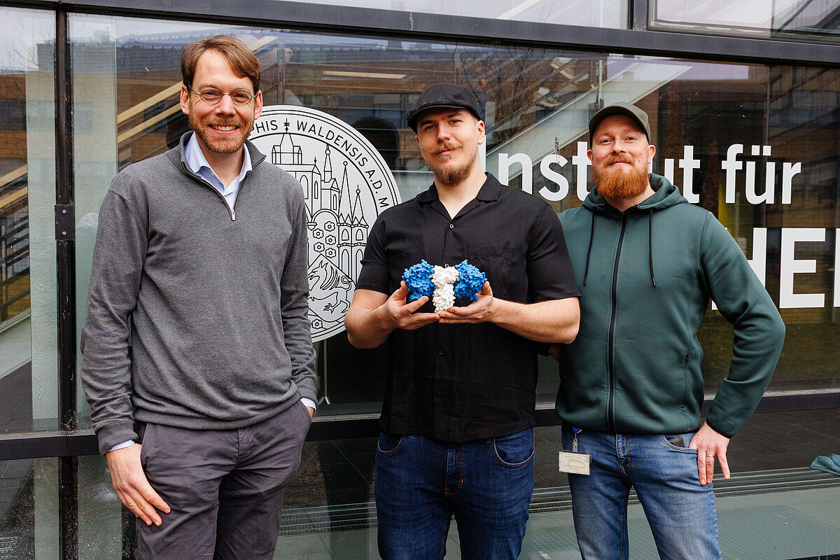 Das Projektteam um Prof. Dr. Michael Lammers, Erstautor Markus Janetzky (M.Sc. Biochemie; präsentiert ein 3D-Strukturmodell des AcuB•AcuC Komplexes) und Zweitautor Norman Geist (MD Simulations Expert).