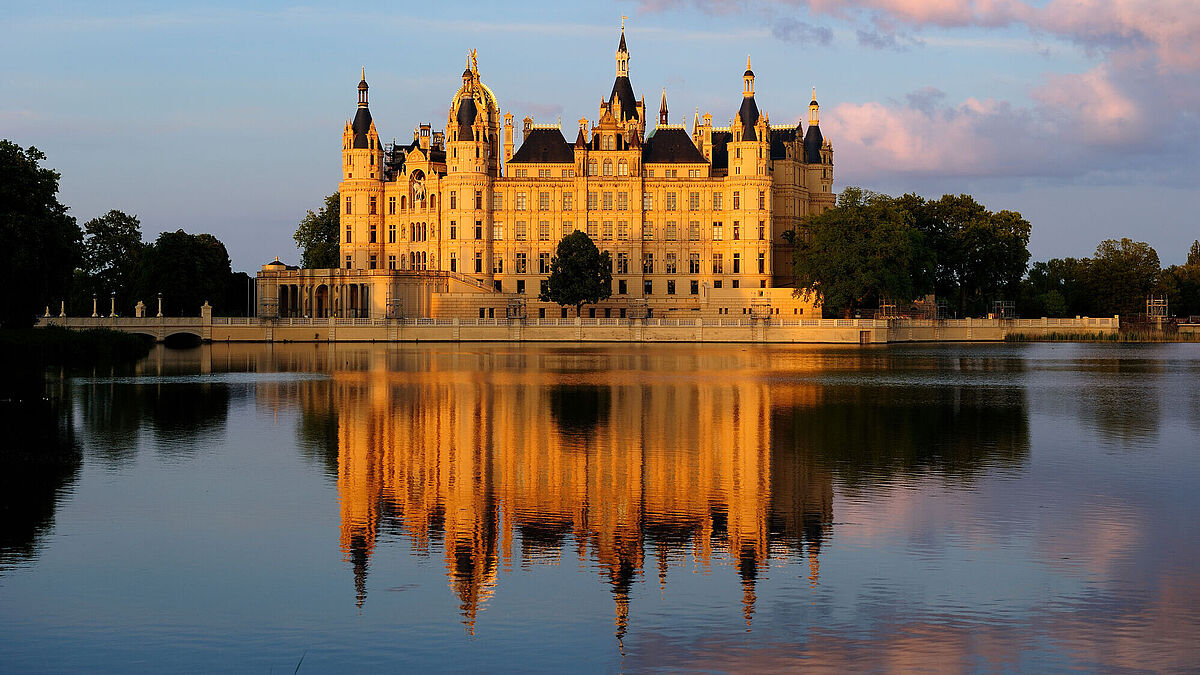 das Schweriner Schloss im Abendlicht. Es spiegelt sich im See.