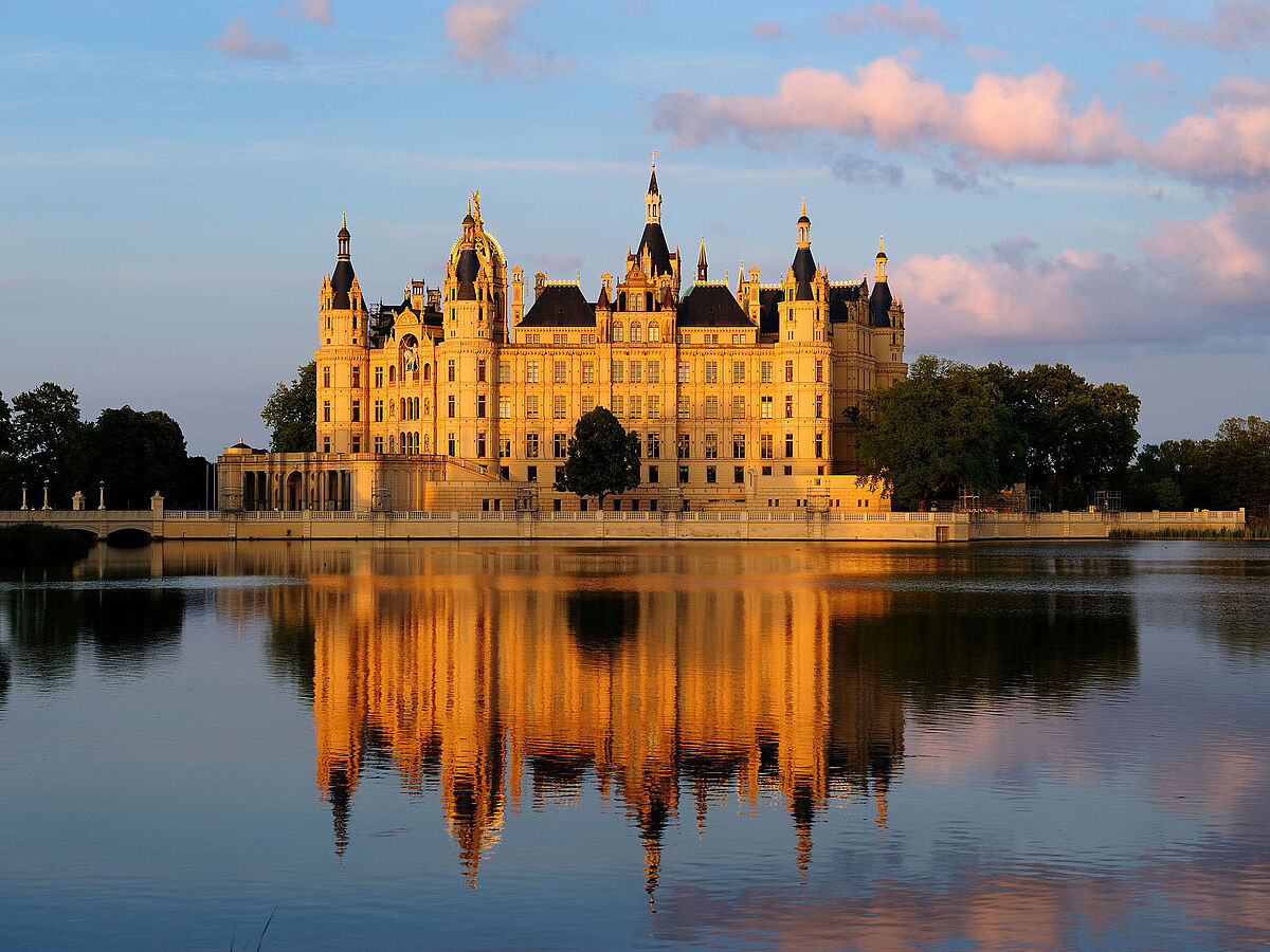das Schweriner Schloss im Abendlicht. Es spiegelt sich im See.