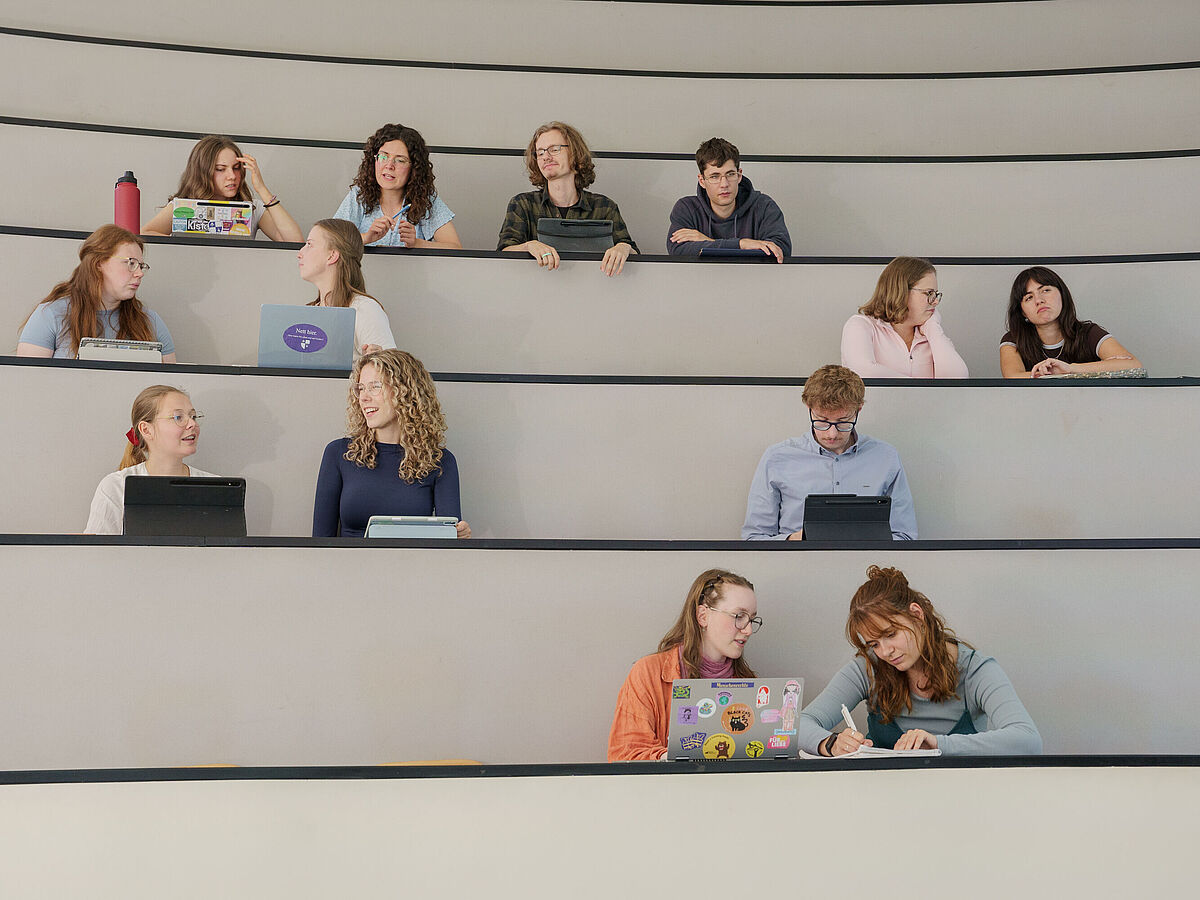 Studierende sitzen in einem Hörsaal und unterhalten sich.