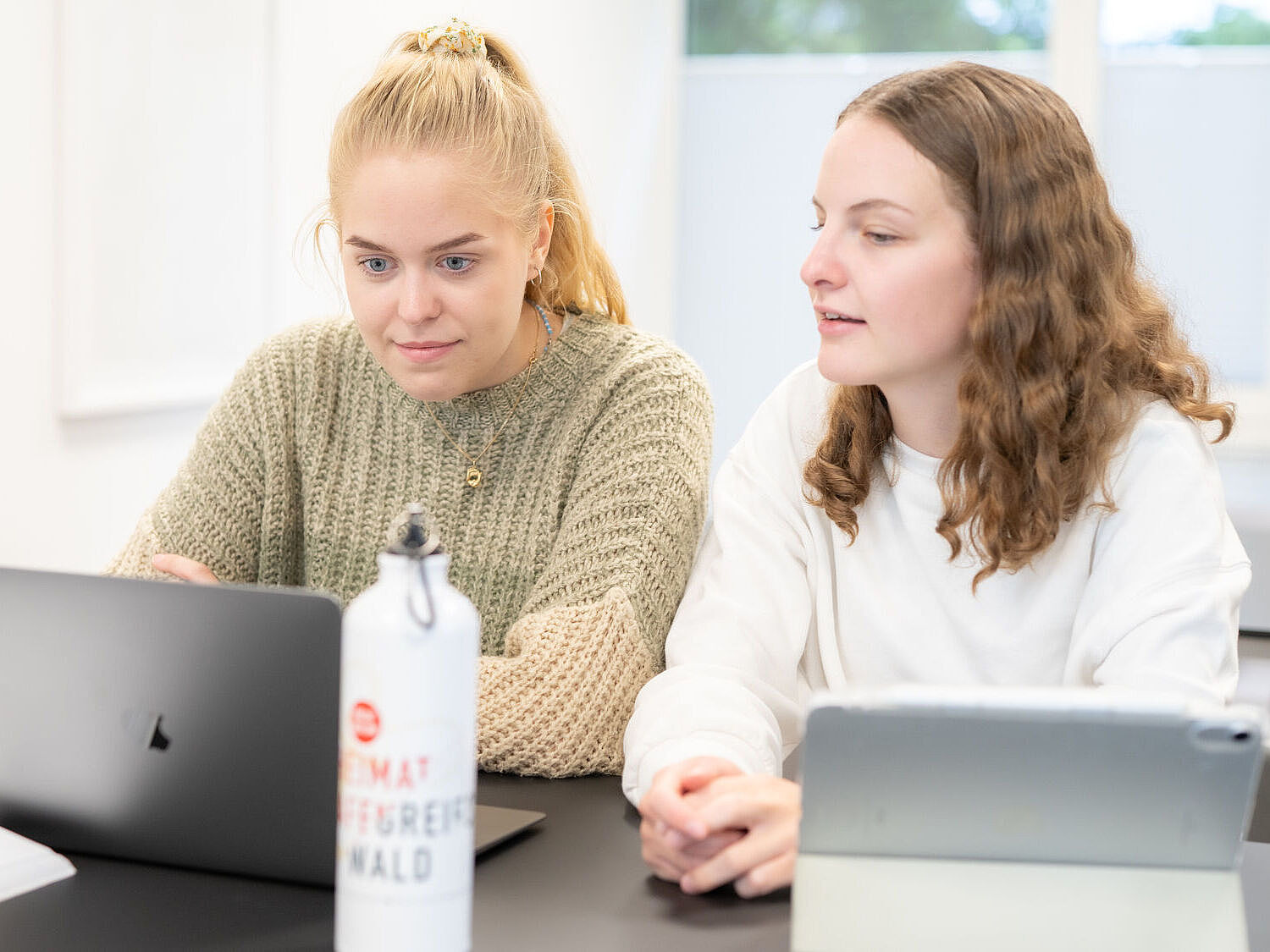 Zwei Studentinnen sitzen nebeneinander an ihren Notebooks und tauschen sich aus.