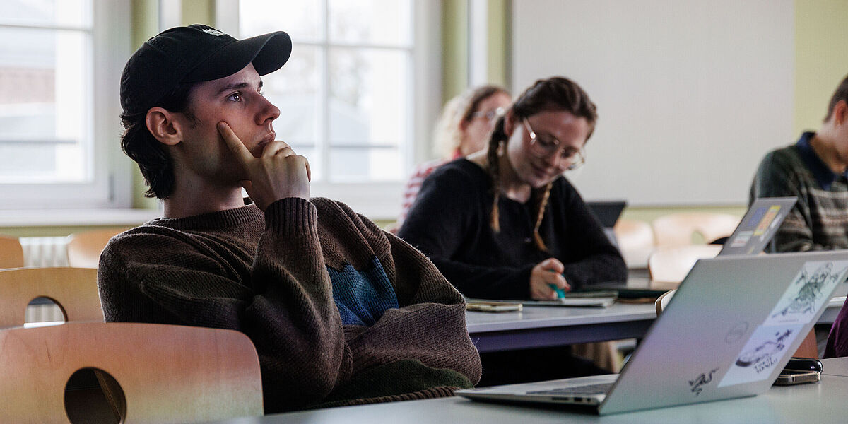 Studierende im Seminarraum bei einem Philosophie-Seminar. Im Vordergrund sitzt ein Student, der ein Basecap trägt.