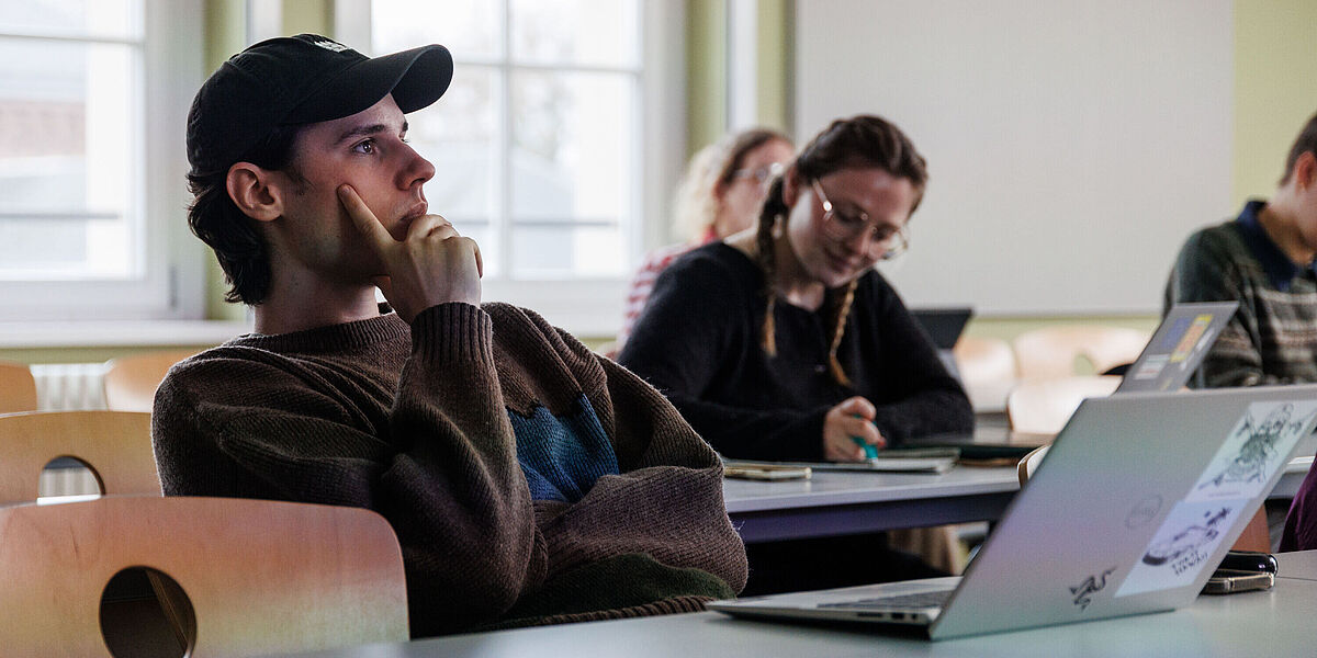 Studierende im Seminarraum bei einem Philosophie-Seminar. Im Vordergrund sitzt ein Student, der ein Basecap trägt.