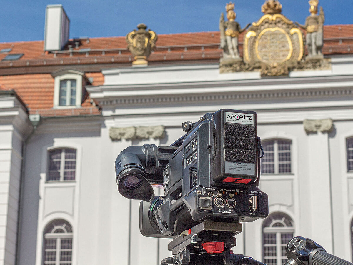 Das Bild zeigt eine Kamera vor dem Universitätshauptgebäude.