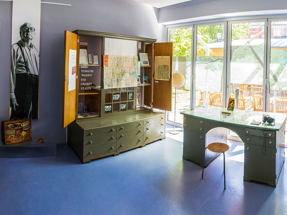 Ausstellungsraum des Koeppen-Archivs mit einem ausgestellten dreiteiligen Stehschrank und einem Schreibtisch. 