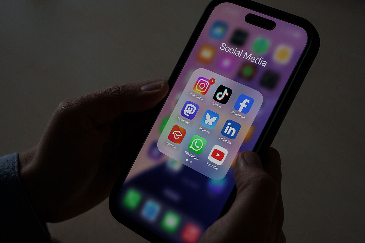 Ein Mann hält ein Handy auf dem verschiedenen Social-Media-Apps geöffnet sind.