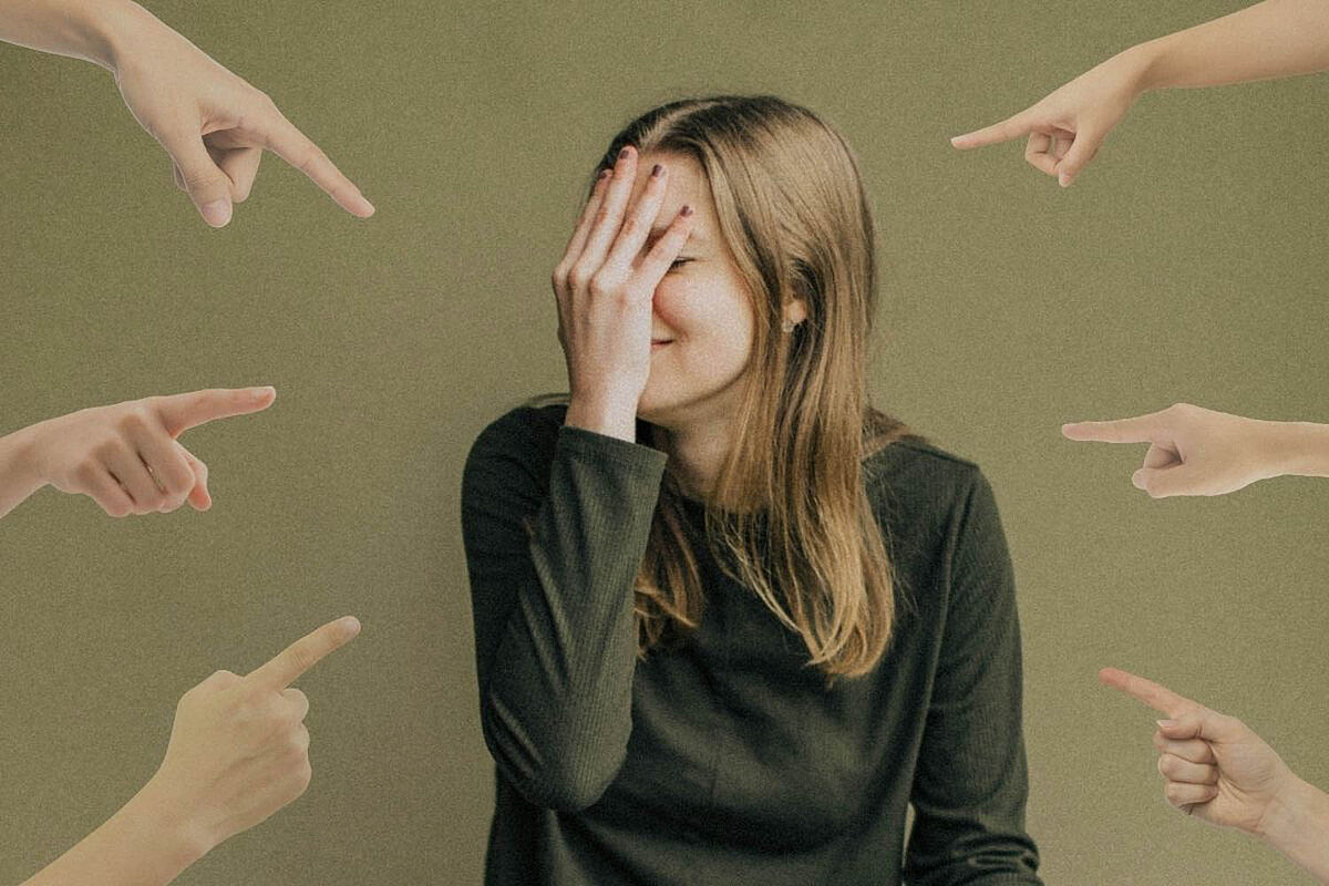 Eine Frau fasst sich peinlich berührt in ihr Gesicht, da sie sich schämt, während viele Finger auf sie zeigen.