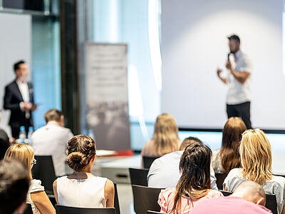 Das Publikum im Saal hört einem Redner zu.