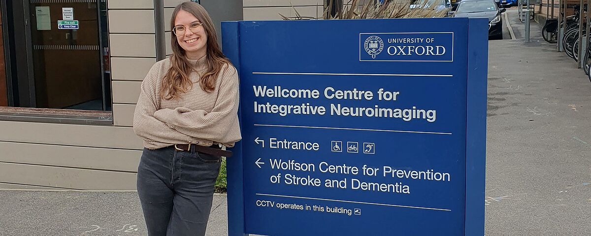 Anna Fromm lehnt an dem Eingangsschild des Zentrums für Integratives Neuroimaging der Universität Oxford