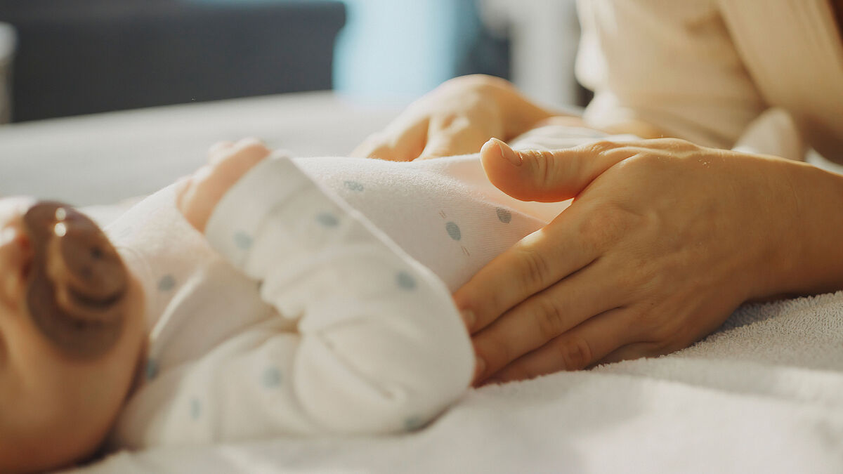 Auf einem Wickeltisch streichelt eine Mutter ihr kleines Baby.
