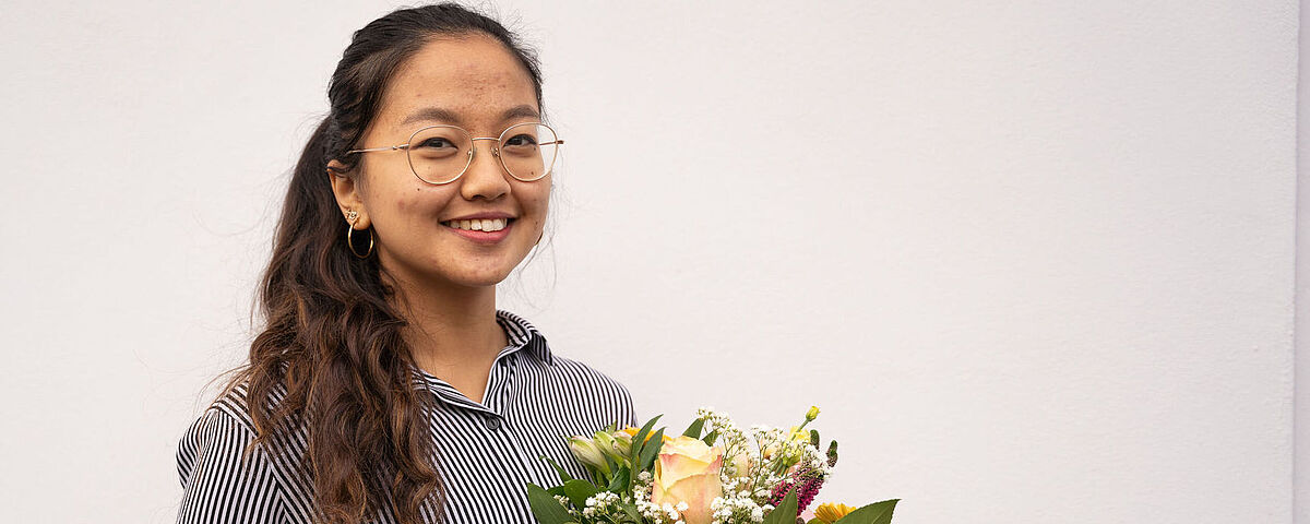 Portrait der DAAD-Preisträgerin 2022, Adventina Padmyastuti mit einem Blumenstrauß in der Hand.