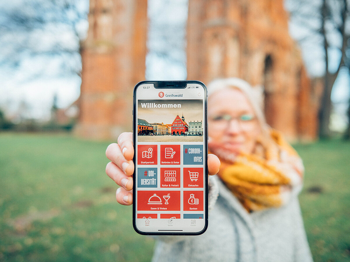 Eine Frau hält ein Smartphone mit der Greifswald App in der Hand.