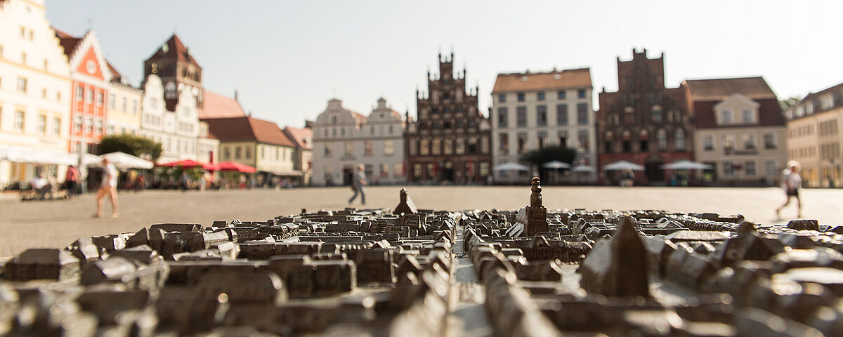 Heimathafen Marktplatz Im Vordergrund sieht man ein gusseisernes Modell der Stadt Greifswald und im Hintergrund die Gebäude des Marktplatzes.