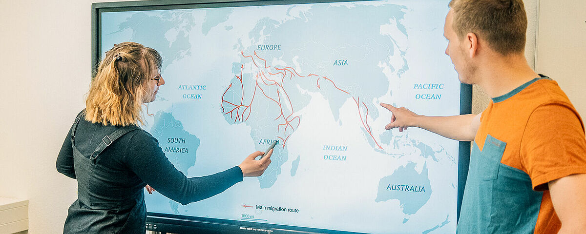 Studierende und Dozent stehen an einer digitalen Karte und sprechen miteinander.