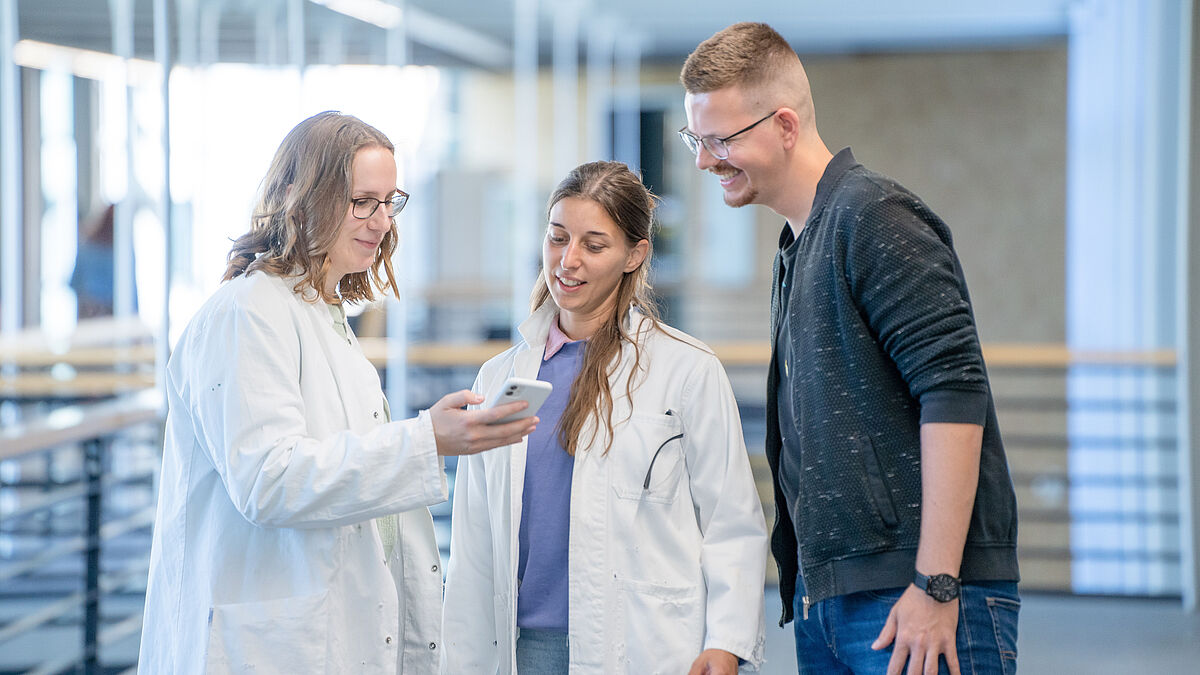 Drei Studierende schauen gemeinsam auf ein Handy 