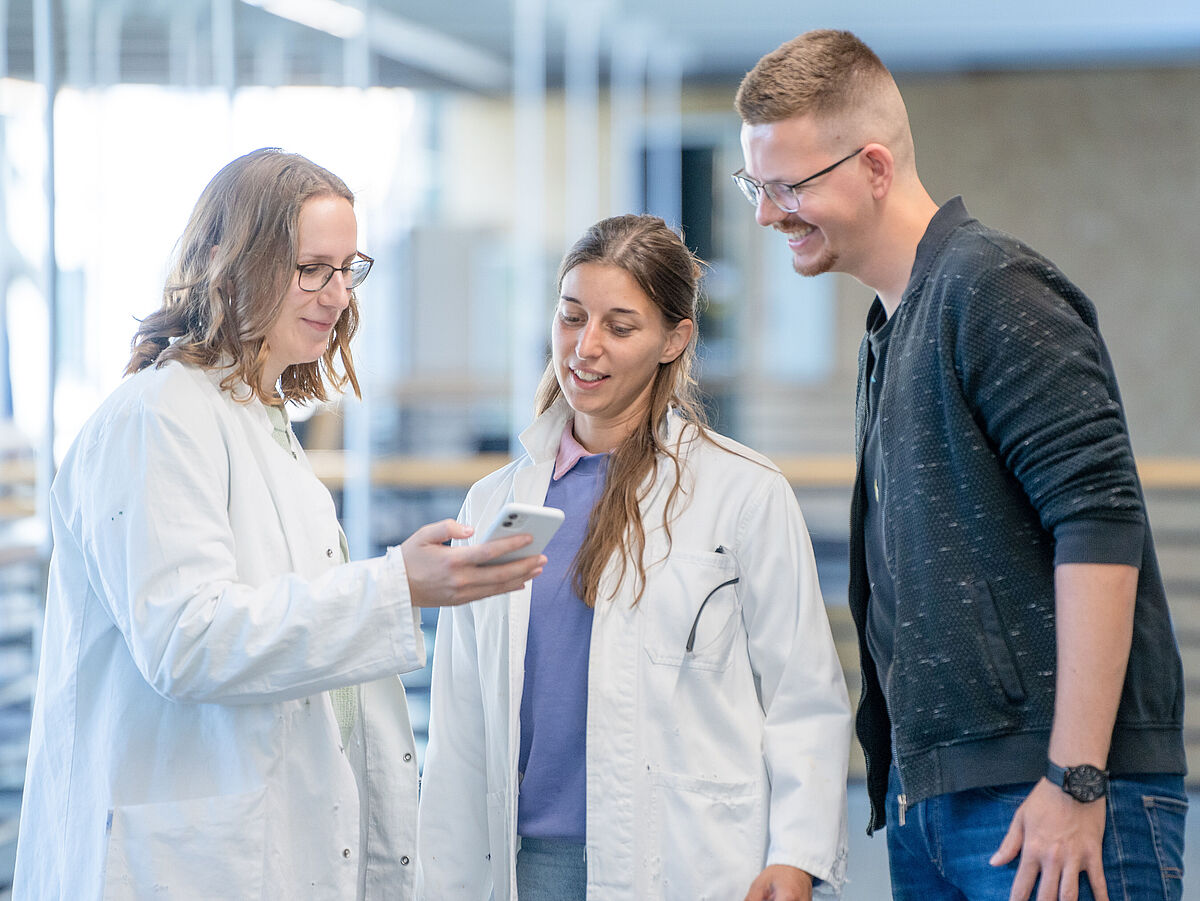 Drei Studierende schauen gemeinsam auf ein Handy 