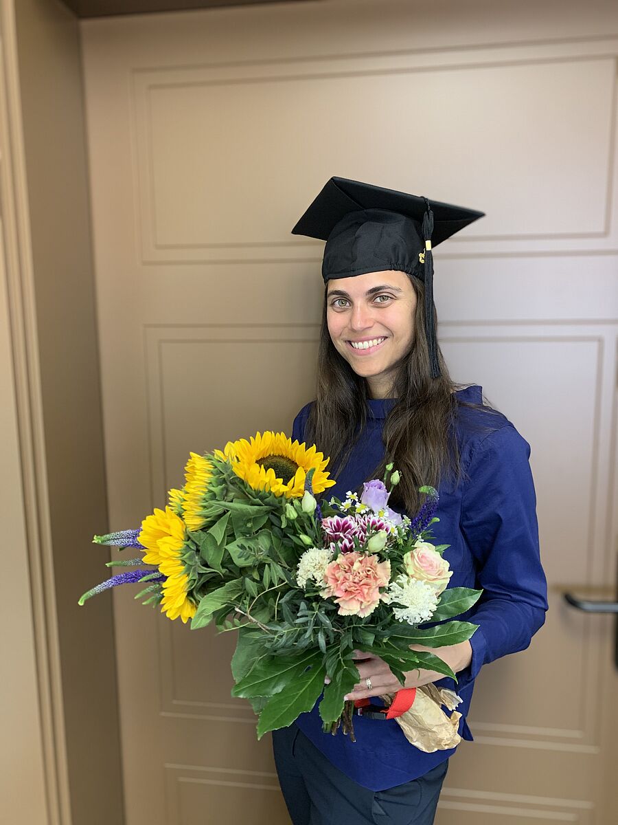 Dr. Lena Varuna Wuntke mit Doktorhut und Blumen in der Hand.