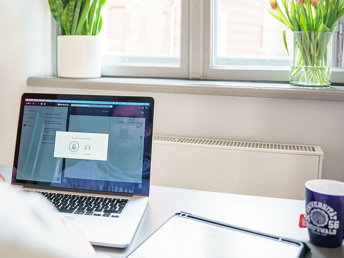 Eine Person sitzt vor einem geöffneten Laptop in einem Online-Meeting.