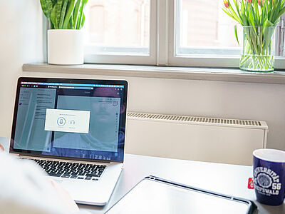 Eine Person sitzt vor einem geöffneten Laptop in einem Online-Meeting.