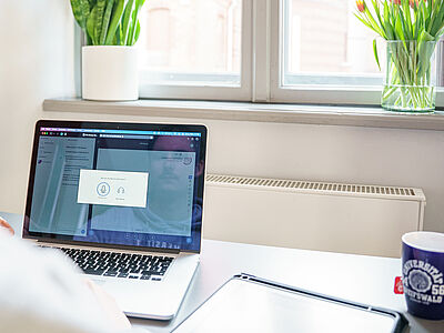 Eine Person sitzt vor einem geöffneten Laptop in einem Online-Meeting.