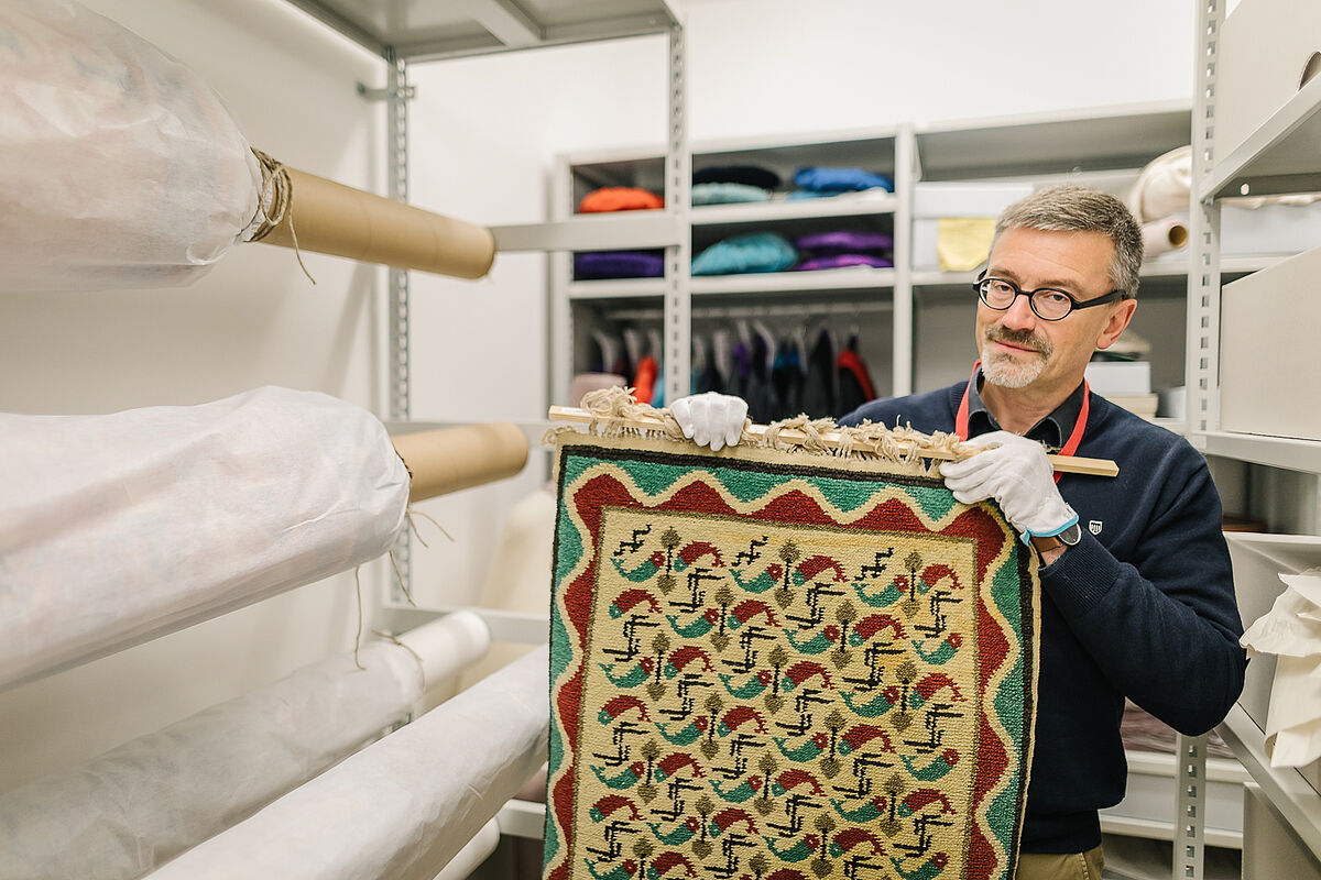 Curator of the University of Greifswald, Dr. Thilo Habel, holding a Pomeranian Fischerteppich by Rudolf Stundl in the storeroom - Photo: Till Junker, 2018