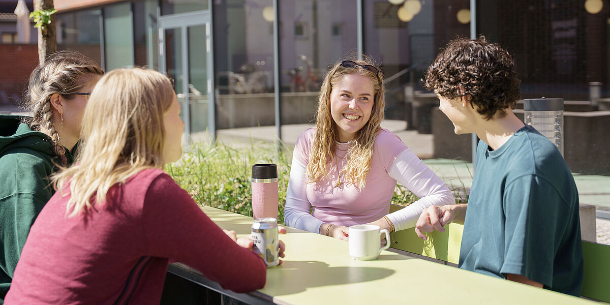 Symbolbild Studieren in Greifswald Eine Gruppe von Studierenden unterhält sich auf der sonnigen Außenterasse der Cafeteria.