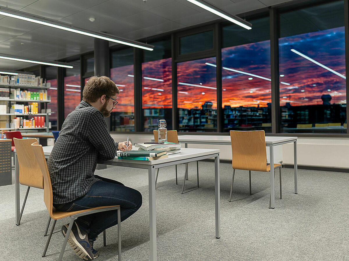 Student am Tisch in der Zentralen Universitätsbibliothek mit Blick auf den Sonnenuntergang über dem Berthold Beitz tz - Foto: Magnus Schult