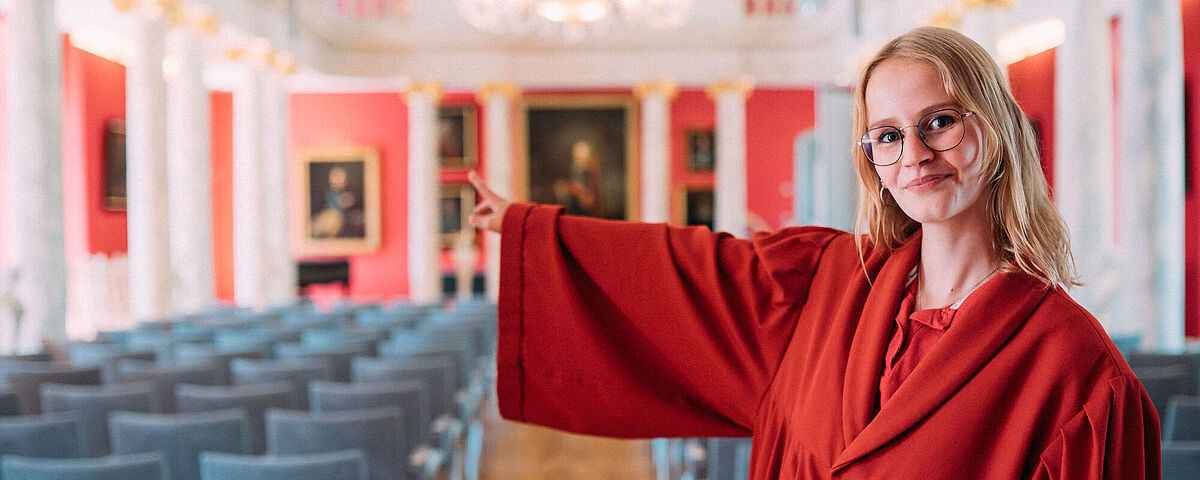 Ein Guide der Kustodie im roten Talar führt durch die Aula der Universität Greifswald.