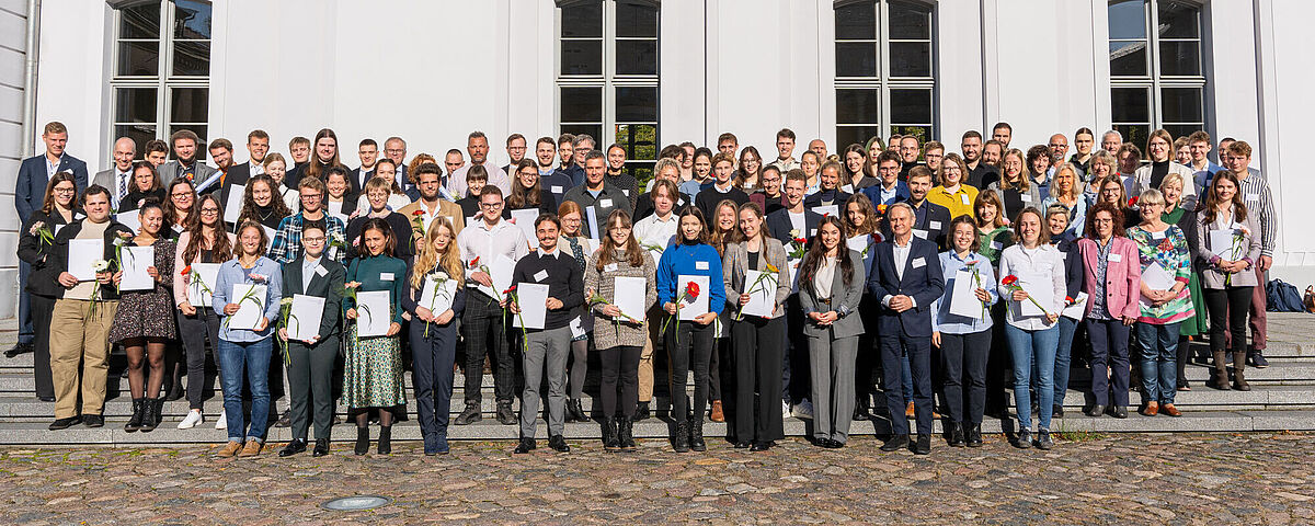 Gruppenbild nach der Vergabe der Deutschlandstipendien 2023. Die Stipendiatinnen und Stipendiaten stehen zusammen mit den Förderinnen und Fördern vor dem Hauptgebäude der Universität. mann, 2023