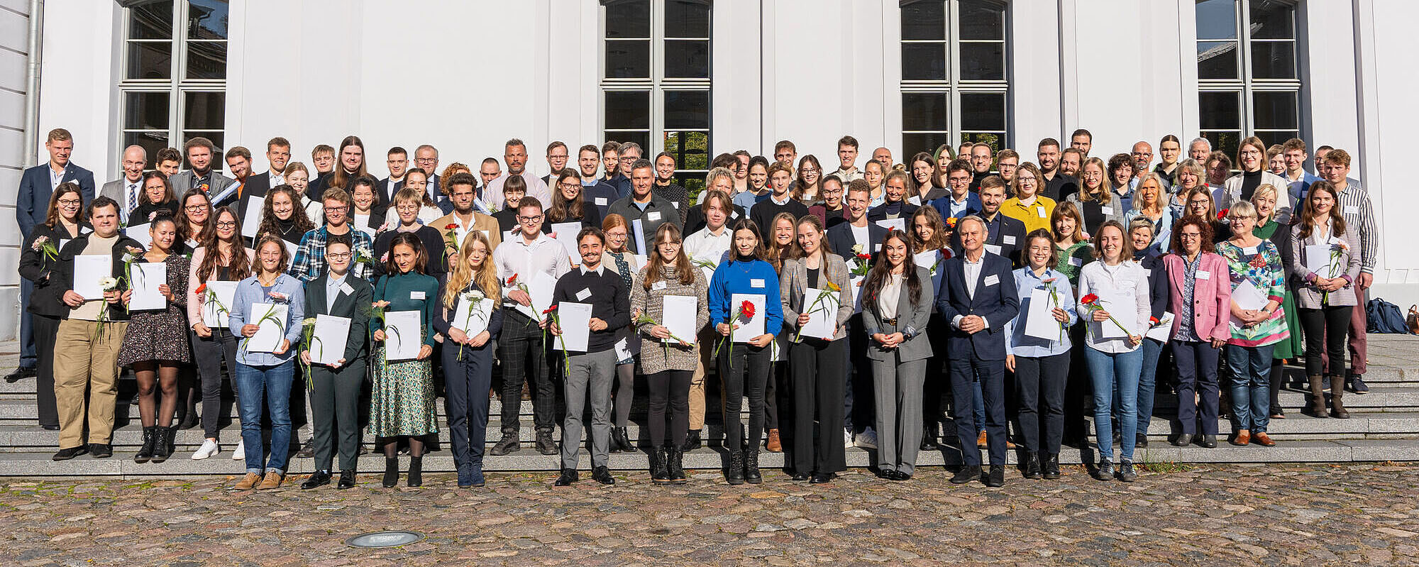 Gruppenbild nach der Vergabe der Deutschlandstipendien 2023. Die Stipendiatinnen und Stipendiaten stehen zusammen mit den Förderinnen und Fördern vor dem Hauptgebäude der Universität. mann, 2023