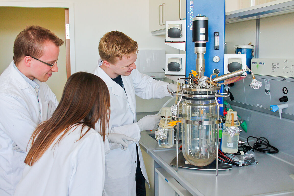 Symbolbild: Drei Personen stehen in einem Labor vor einer Apparatur 