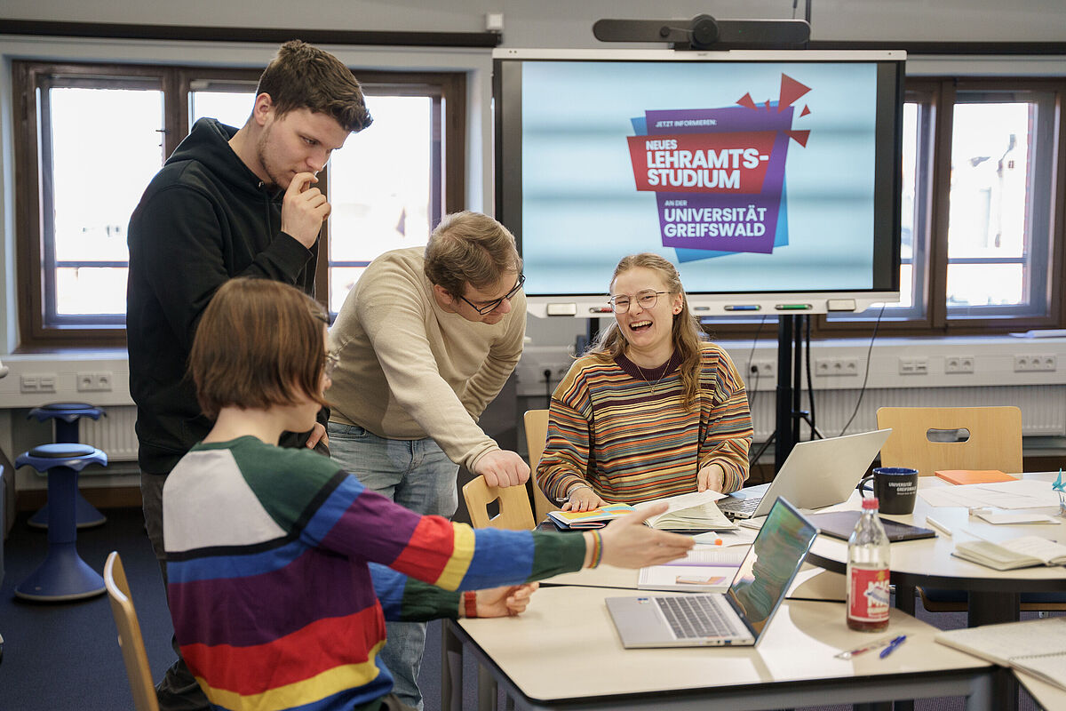 Kampagne neue Lehramtsstudiengänge Eine Gruppe Lehramtsstudierende diskutiert in einem Seminarraum. Vor ihnen liegen geöffnete Hefte und Bücher sowie Laptops.