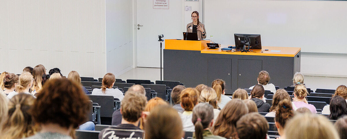 Eine Frau hält einen Vortrag in einem Hörsaal, in dem sehr viele Menschen sitzen.