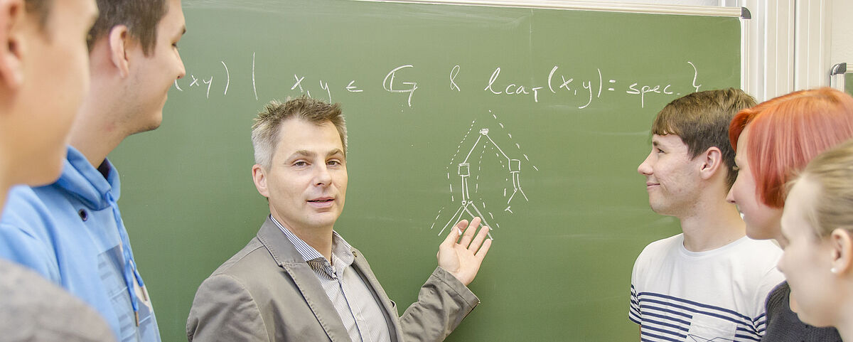 Mehrere Personen stehen vor einer Tafel, auf der mathematische Formeln abgebildet sind.