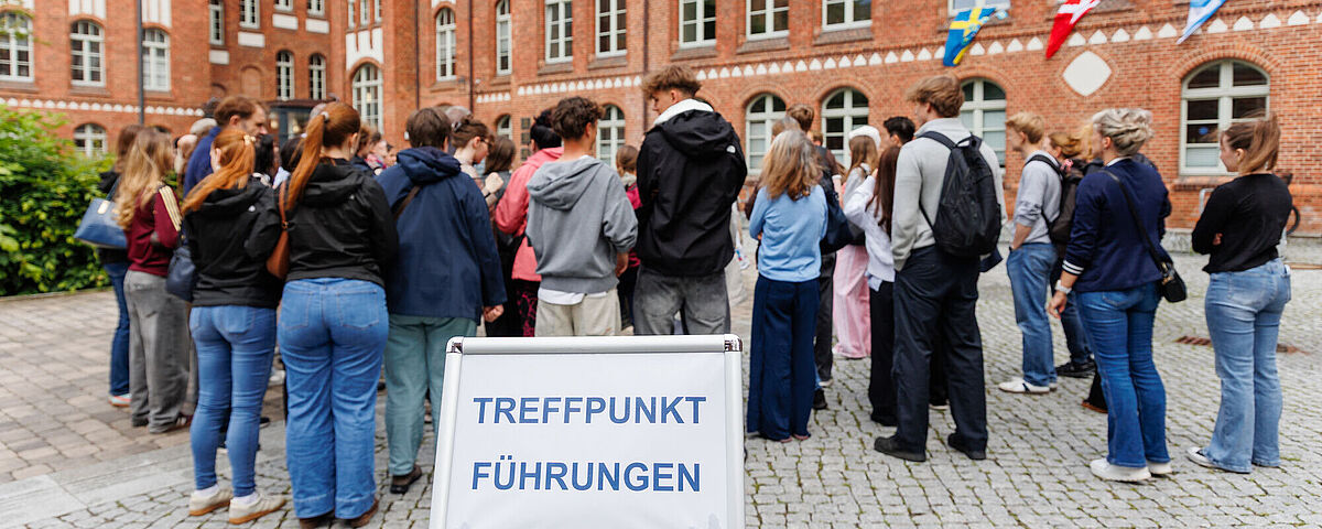 Viele Menschen stehen hinter einem Schild, auf dem "Treffpunkt Führungen" steht.