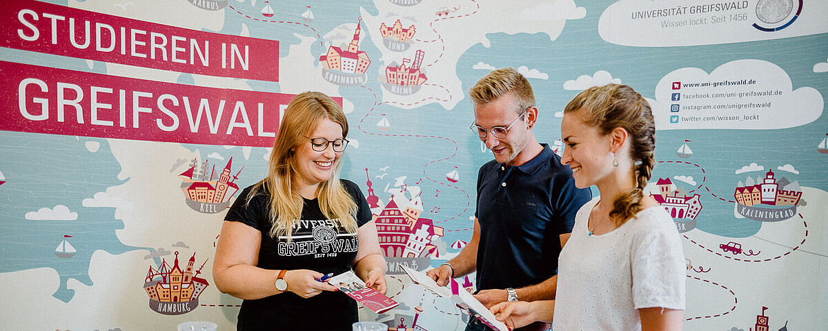 Zwei Personen werden an einem Infostand von einer anderen Person über Studienmöglichkeiten informiert.