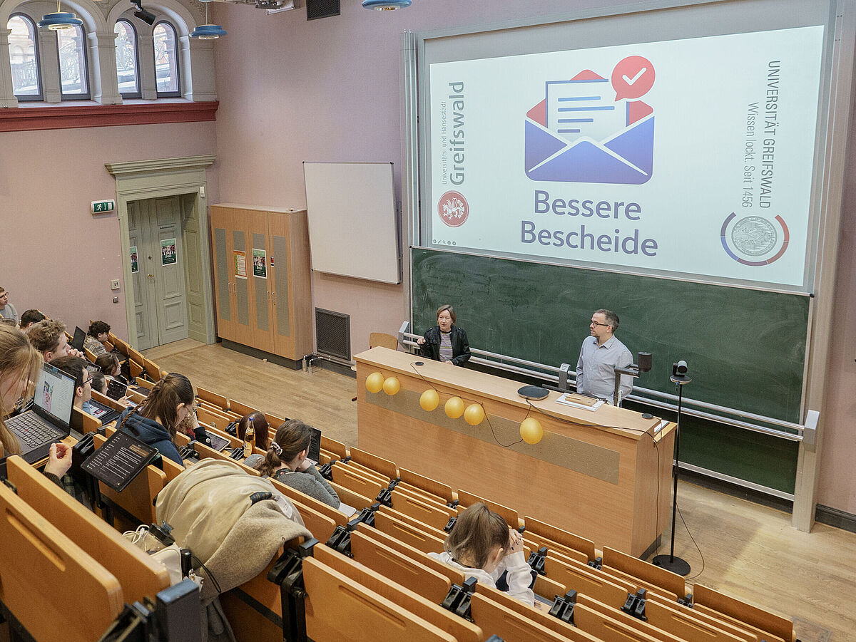 Mehrere Personen sitzen im Hörsaal und hören den Dozierenden zu.