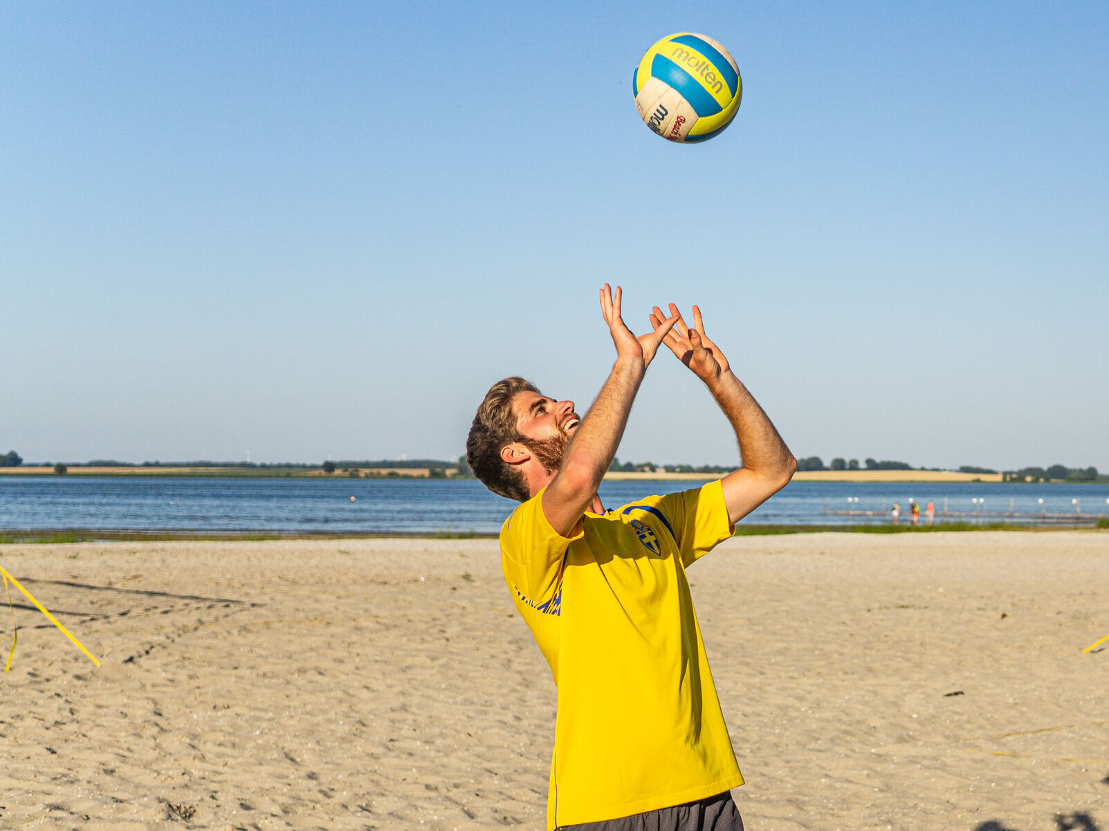 Eine Person spielt am Strand mit einem Volleyball.